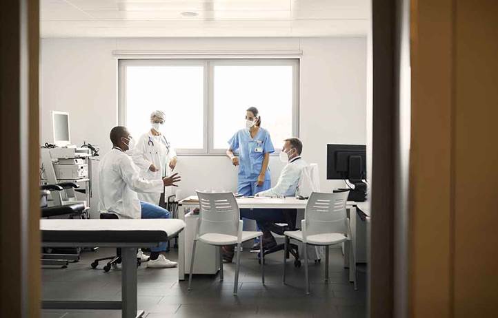 Group of hospitals and nurses talking in hospital room.