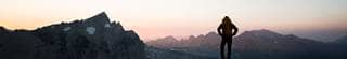 Backpacker summiting a mountain, looking out over a sunset.