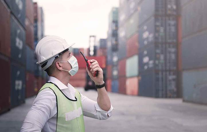 Worker in a hard hat, wearing a mask, talking into a walkie talkie