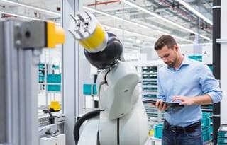 Business professional in casual clothing standing next to an automated robot.