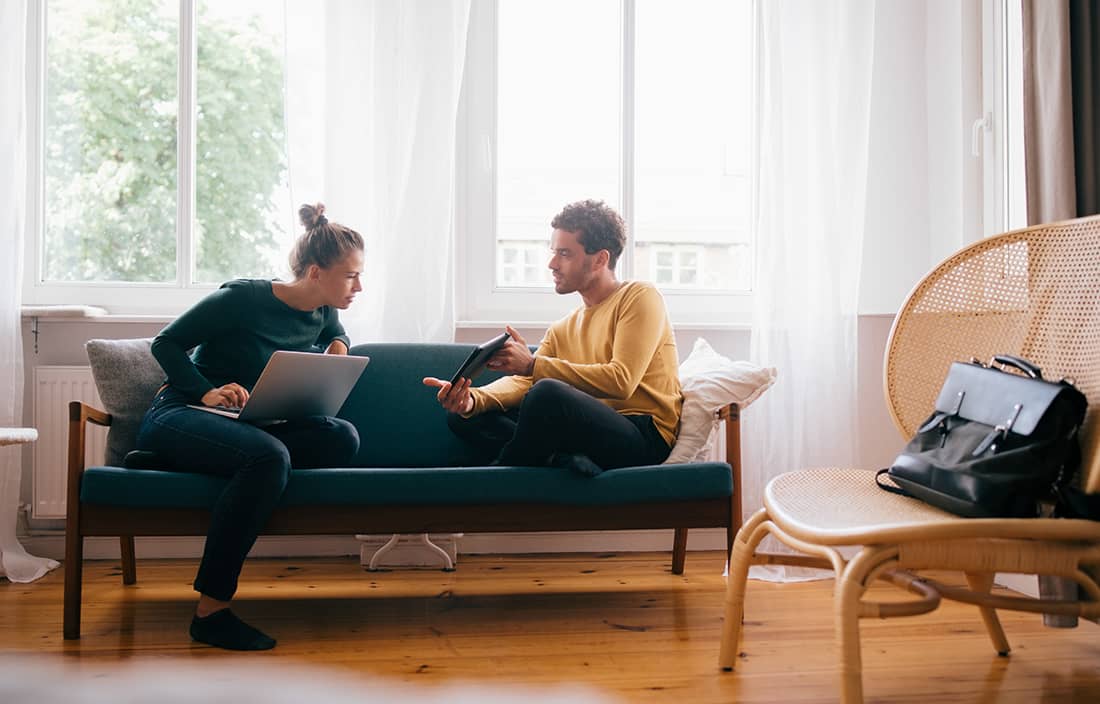 Two people sitting on a couch and reviewing their investments on their computer.
