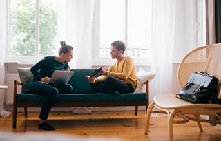 Two people sitting on a couch and reviewing their investments on their computer.