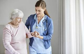 Nurse helping senior citizen walk across the room.