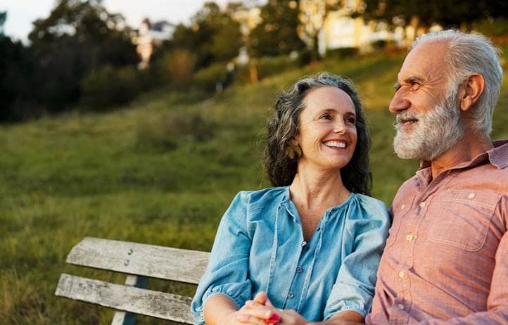 Senior couple smiling and talking to each other on a bench.
