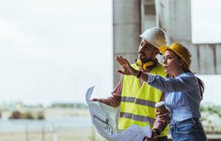 Construction professionals in hardhats and hi-vis jackets reviewing blueprints.