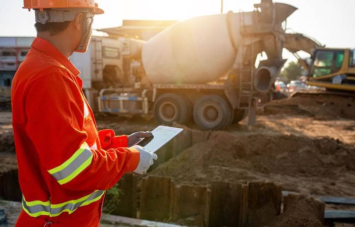 Construction worker holding a clipboard while looking a concrete mixing machine