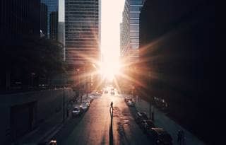 Aerial view of a city street bracketed by skyscrapers at sunset with the sun peaking between the buildings