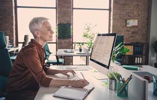 Professional real estate consultant, an older lady, sitting at a computer in an office