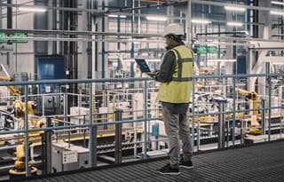 Manufacturing worker on a laptop by machinery in a factory