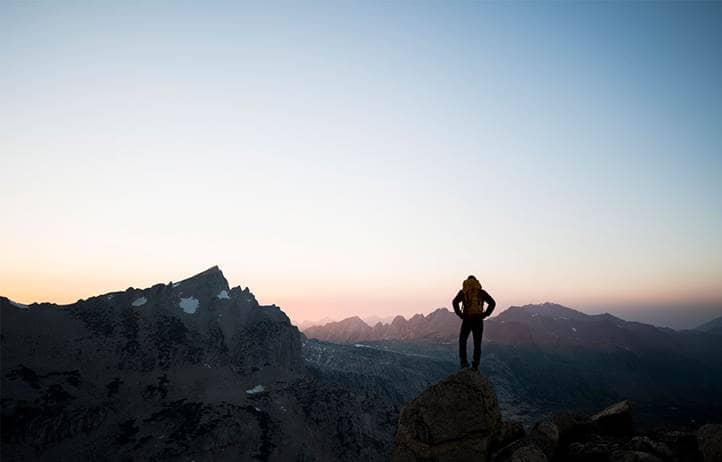Backpacker summiting a mountain, looking out over a sunset.