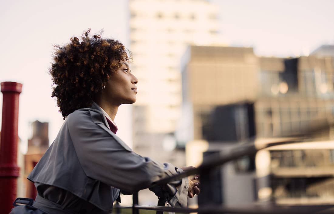 Woman looking contemplative on a rooftop with city skyline background