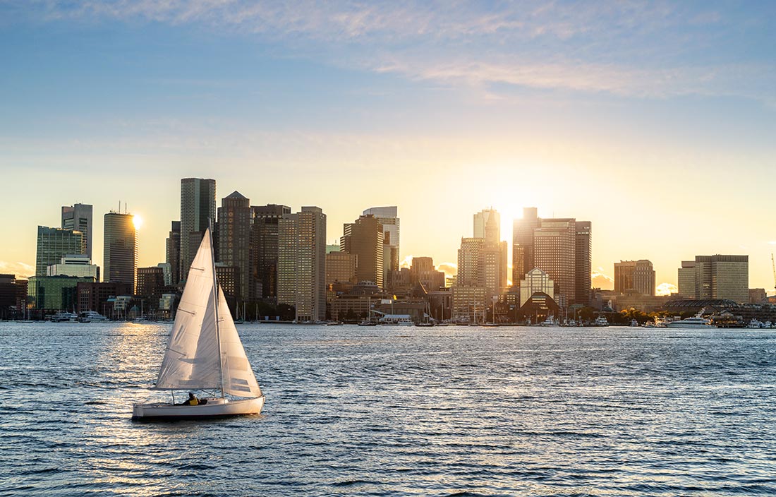 Sailboat with a Boston skyline seen during sunset in the background