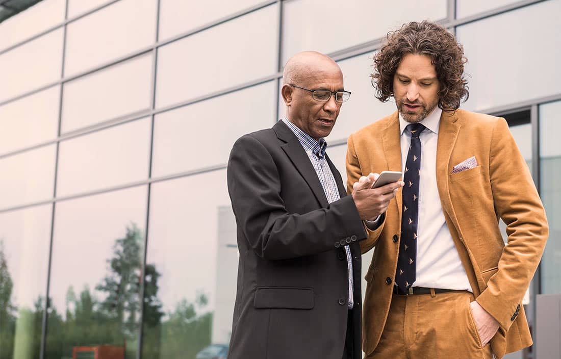 Two businessmen talking about a real estate investment transaction, looking at information on a phone