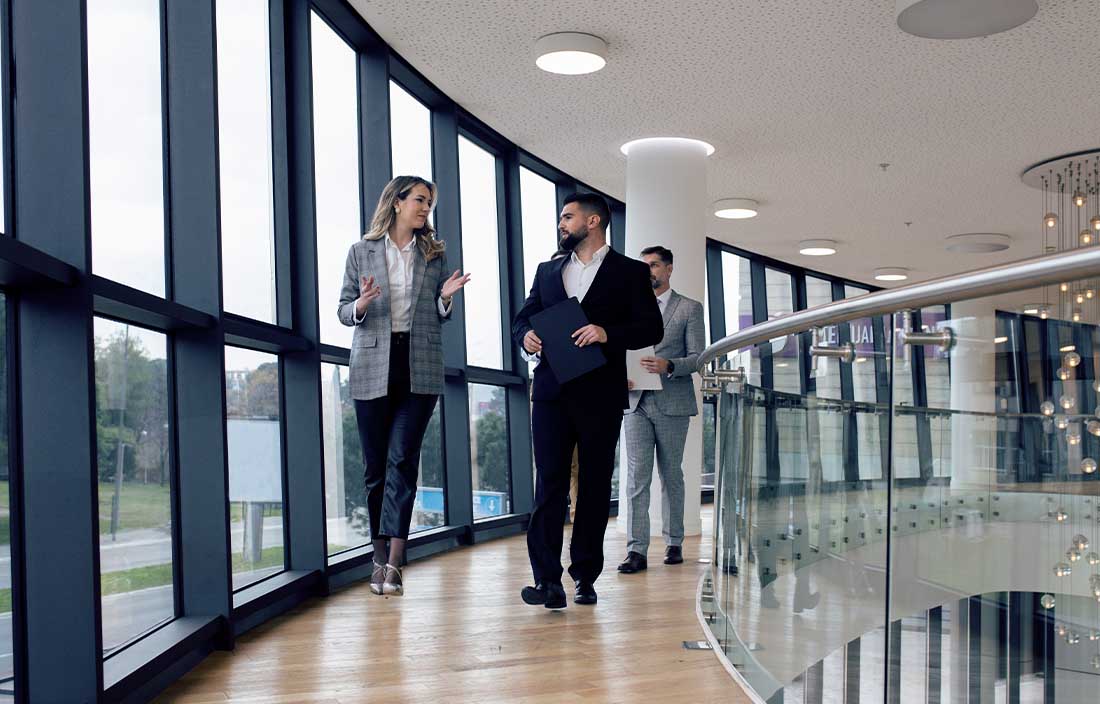Man and woman walking in an office hallway and talking to each other.