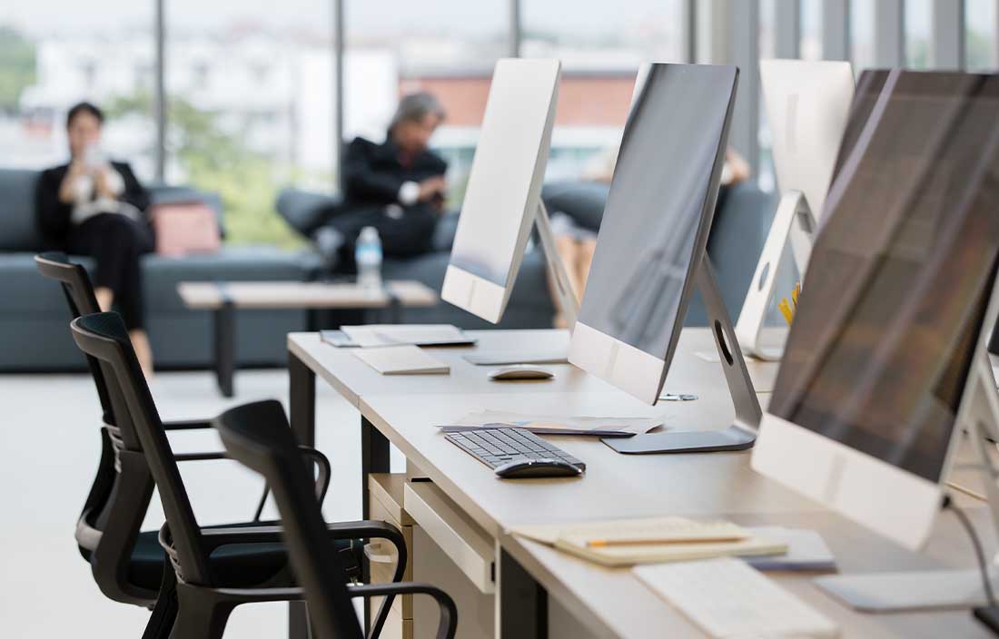 Computer monitors in an office with people in the background.