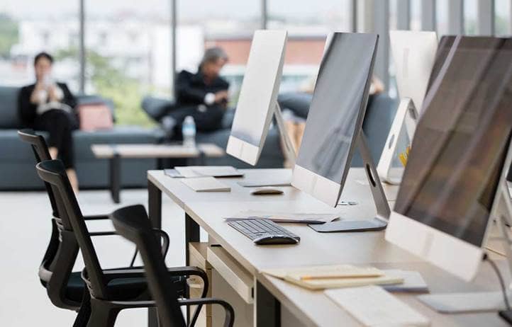 Computer monitors in an office with people in the background.