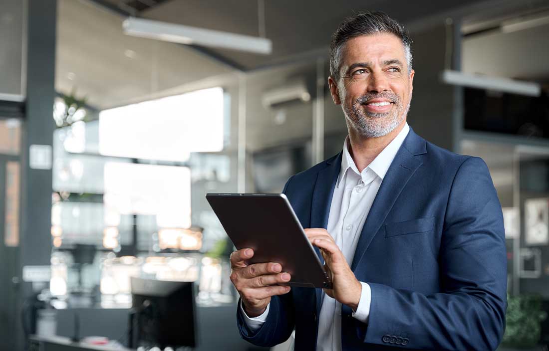 Man in a suit holding a tablet and looking to the side.