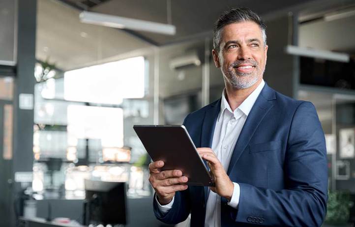 Man in a suit holding a tablet and looking to the side.