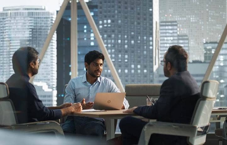 Three men talking in an office building in a city.