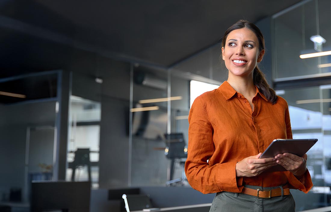 Woman holding a tablet in an office looking to the side.