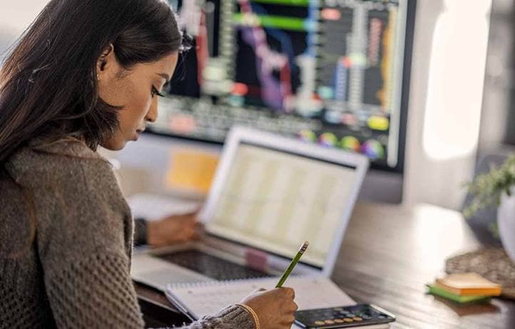 Woman sitting at her computer looking at economic data and calculating potential investment opportunities